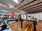 Een showroom met een deel van een houten sporthalvloer. Daarop staat een tafel met een blad van diezelfde vloer. Aan weerskanten staan een lichtblauwe en een gele stoel.
